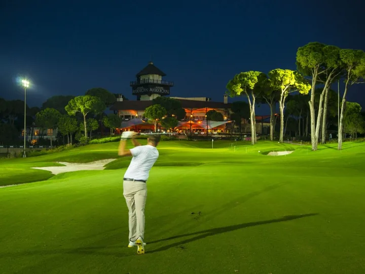 A golfer playing under floodlights beside the Montgomerie Maxx Royal clubhouse in Belek